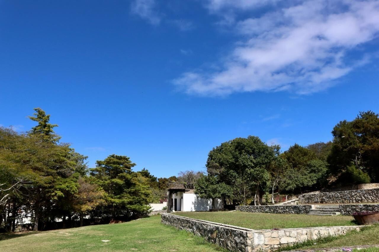 A stone wall with a small building, surrounded by trees and grass.