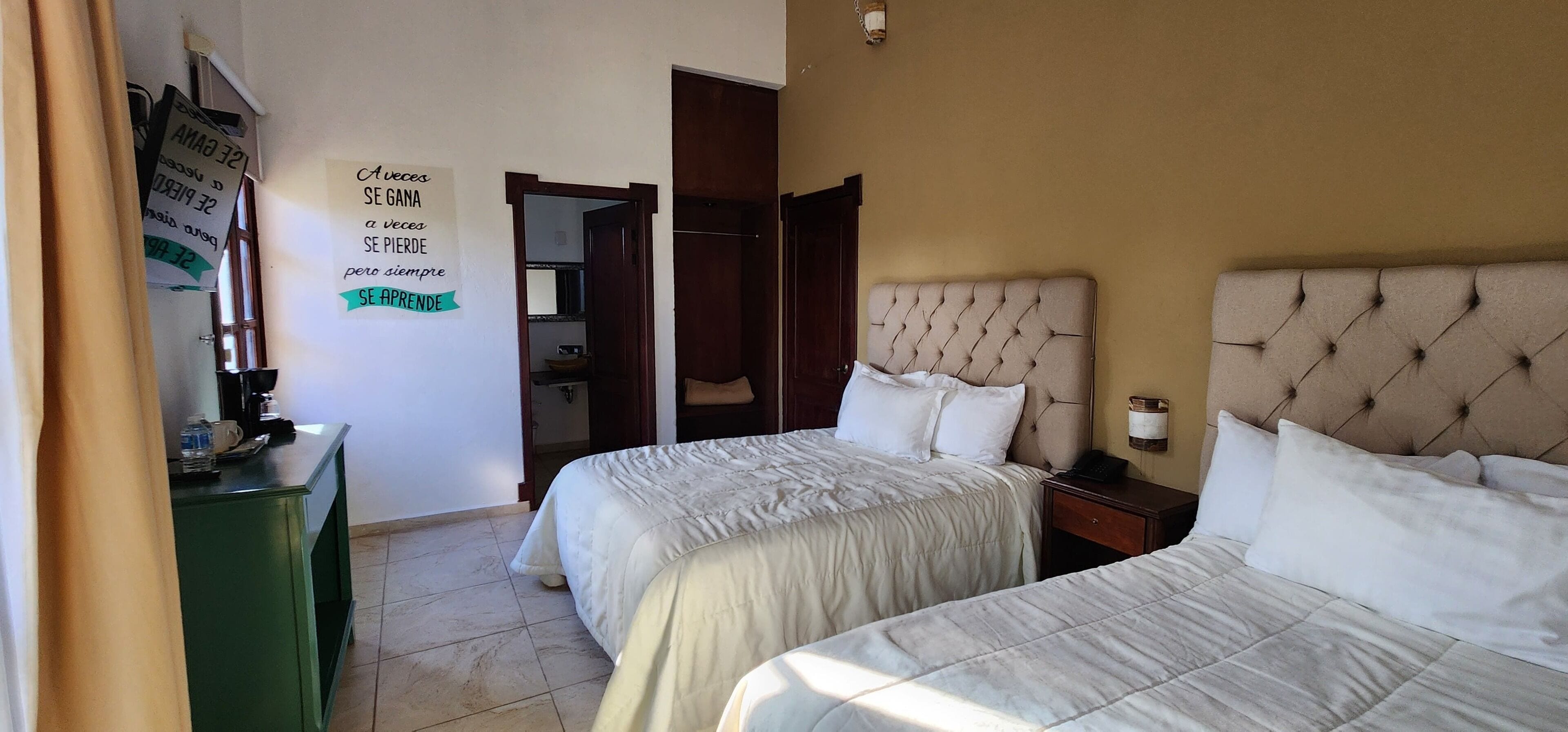 A hotel room with two beds, a green desk with a telephone, and a mirror.