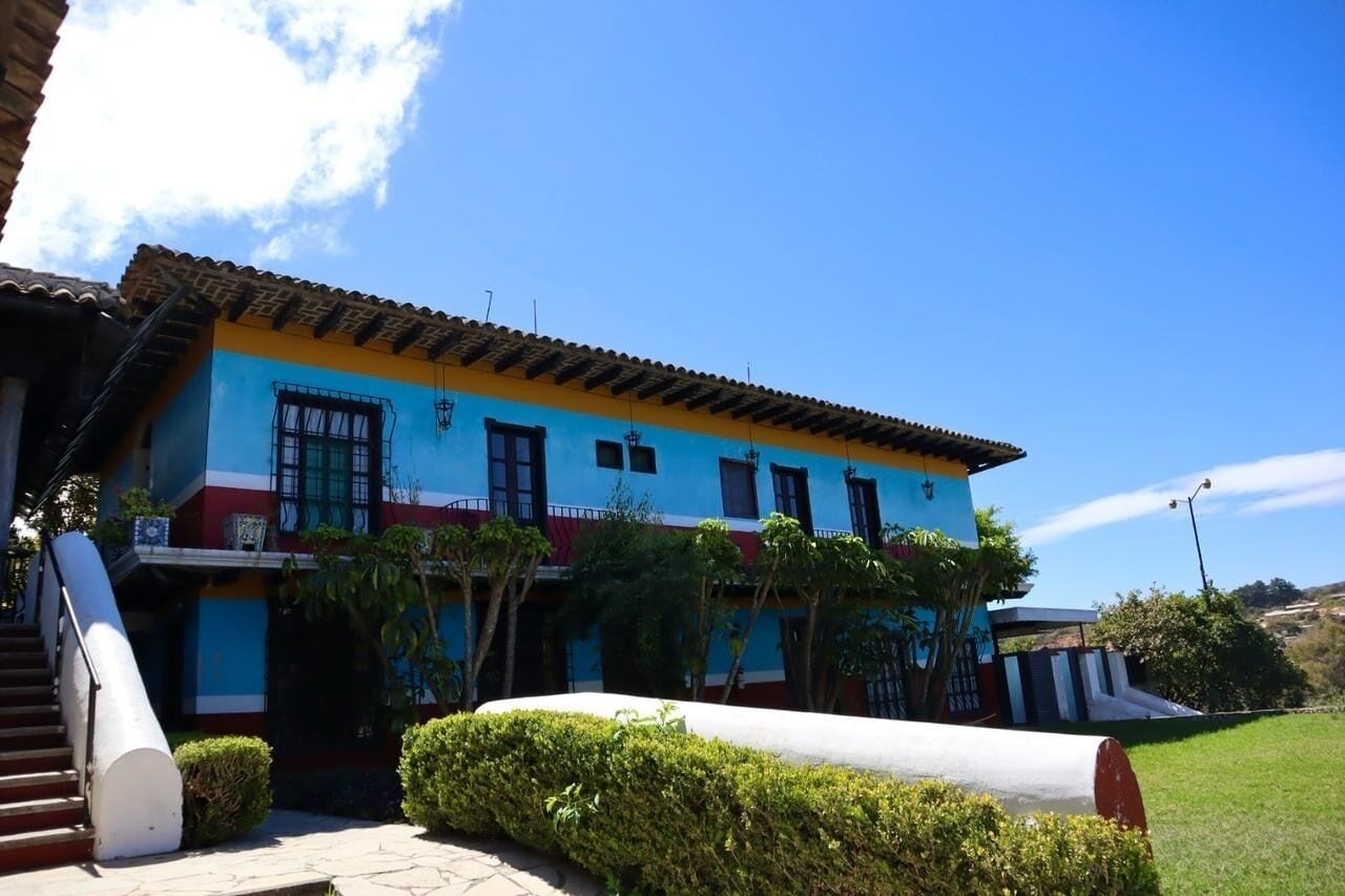 Un edificio colorido con fachada azul y amarilla, una escalera y un jardín bien cuidado.