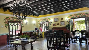 Un comedor con mesas y sillas de madera, una lámpara de araña y adornos florales en las paredes.