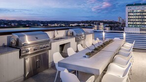 An outdoor kitchen with a grill, sink, and bar seating on a rooftop with a view of the city.