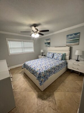 Cozy retreat with a central bed, ceiling fan, and window with blinds.