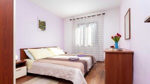A bedroom with two beds, a wooden desk, a nightstand, a bedside table, a framed picture on the wall, and a window with sheer curtains. - ADRIA One-Bedroom Apartment with Balcony 2 (Rovinj)