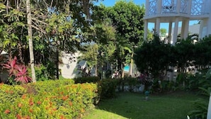 A lush garden with a variety of plants and a white building with a balcony. - Relax with us Casa de Columbus!
5- mins from the beach and other fun activities! (Ocho Rios)