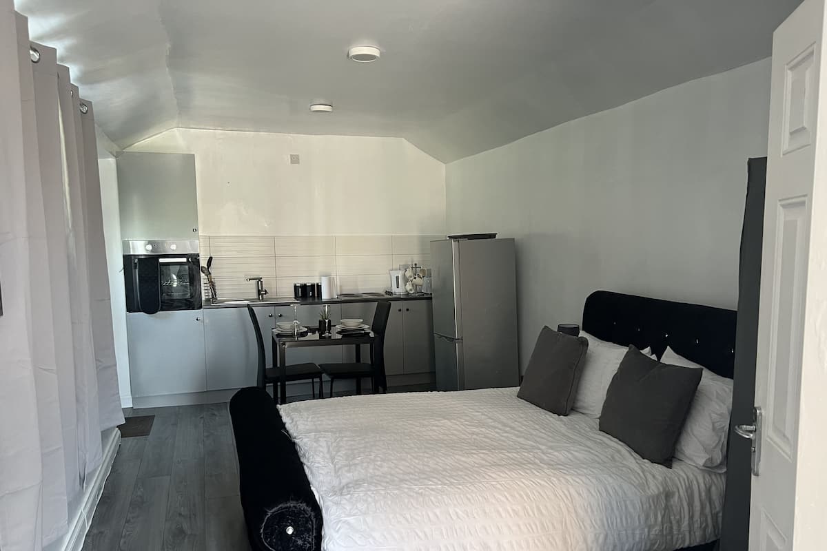 Quarto de hotel compacto com cama, pequena cozinha e área de refeições.