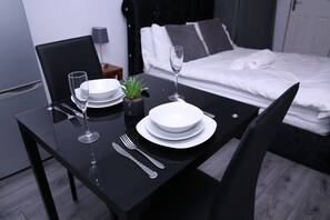 A neatly set dining table with plates, cutlery, and a wine glass in a modern room with a bed in the background. - The Lodge Oldham (Oldham)