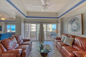 A spacious living room with leather sofas, a glass coffee table, and a ceiling fan.
