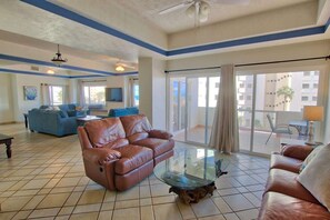 A spacious living area with a brown leather sofa, a glass coffee table, and a blue sofa.