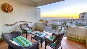 A balcony with wicker furniture, a glass table, and a view of the beach and buildings. - Delphin 403A, Las Palmas Resort (Puerto Peñasco)