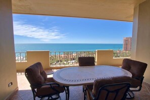A balcony with a round table and four chairs, overlooking a beach and ocean.