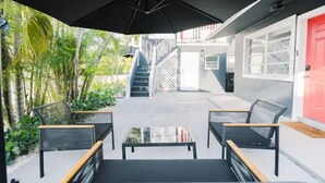 Un espace extérieur aménagé avec une table et des chaises, une porte rouge et un escalier menant à un niveau supérieur.