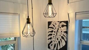 Une chambre à coucher comprenant un lit, deux luminaires suspendus, une fenêtre avec des stores et une œuvre d’art accrochée au mur.