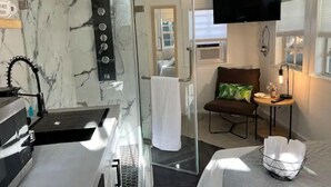 Une chambre d’hôtel équipée d’une douche, d’un lit, d’une télévision, d’une petite table avec une lampe et d’une chaise.