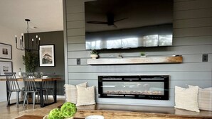 A modern living room with a fireplace, a dining area, and a TV mounted on the wall.