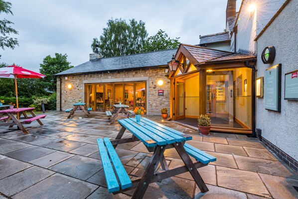 An outdoor patio with stone flooring and wooden picnic tables.