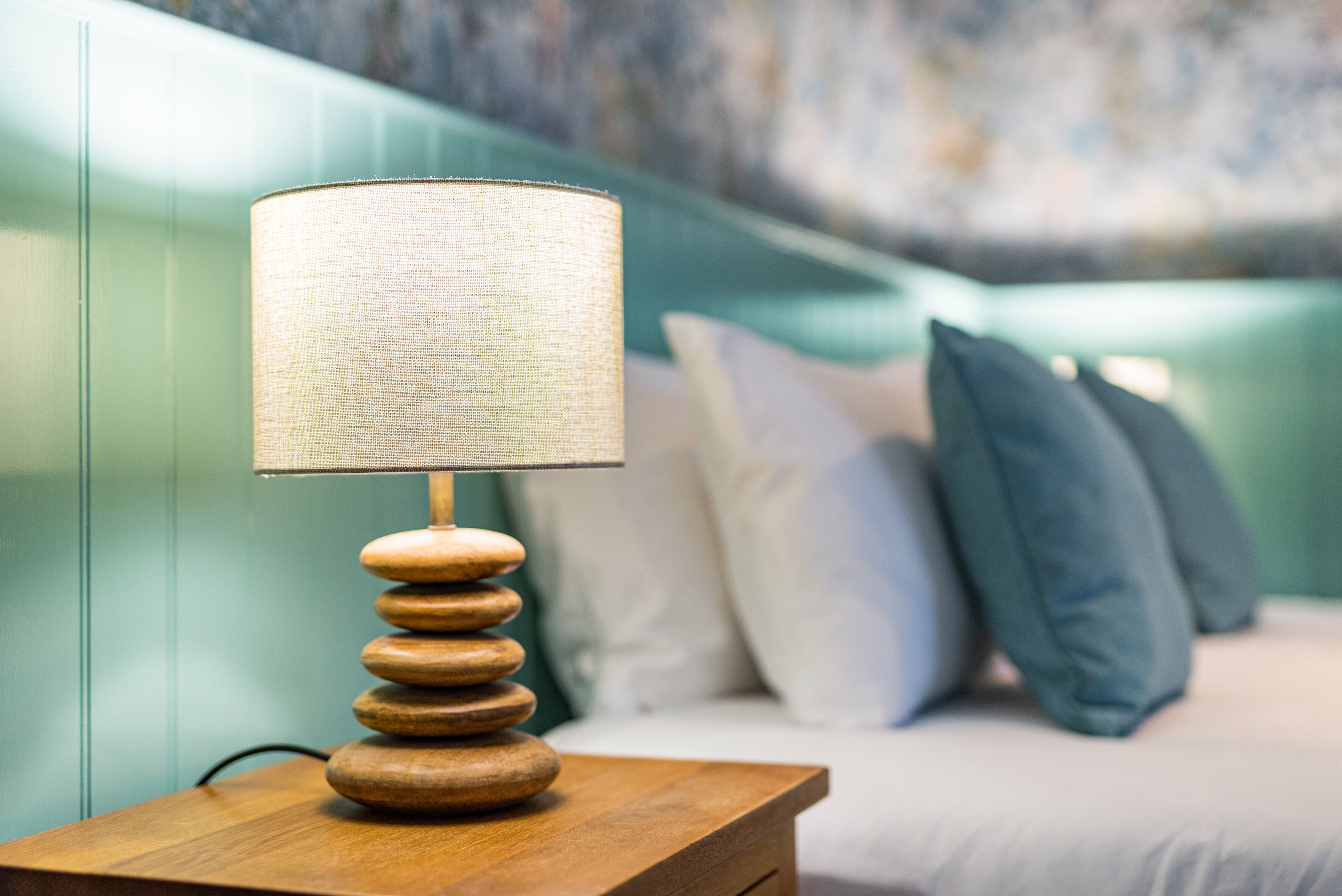 A wooden bedside table with a lamp, a bed with pillows, and a green wall in the background.