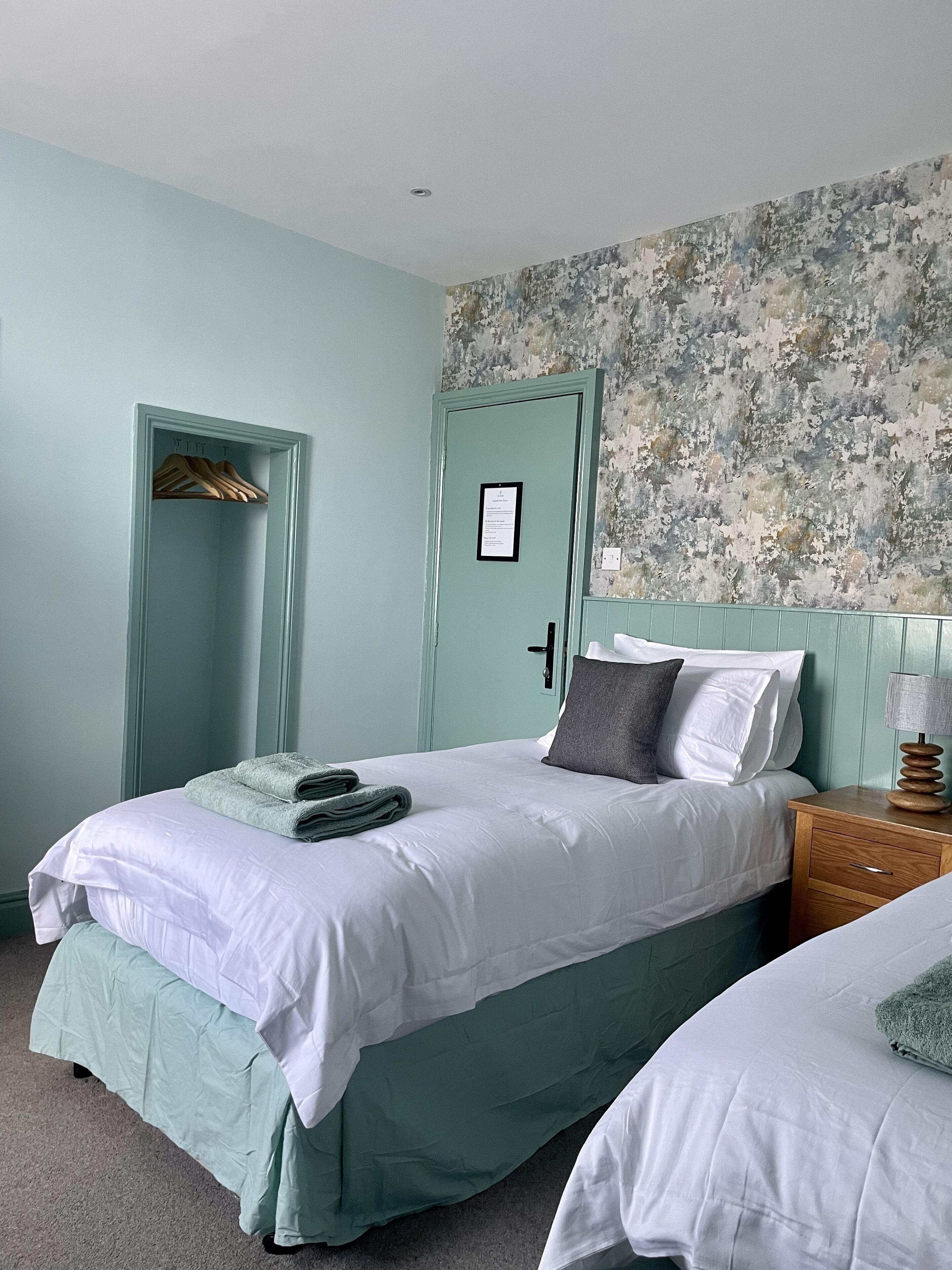 A bedroom with a bed, a wooden nightstand, a door, and a wall with a distressed pattern.