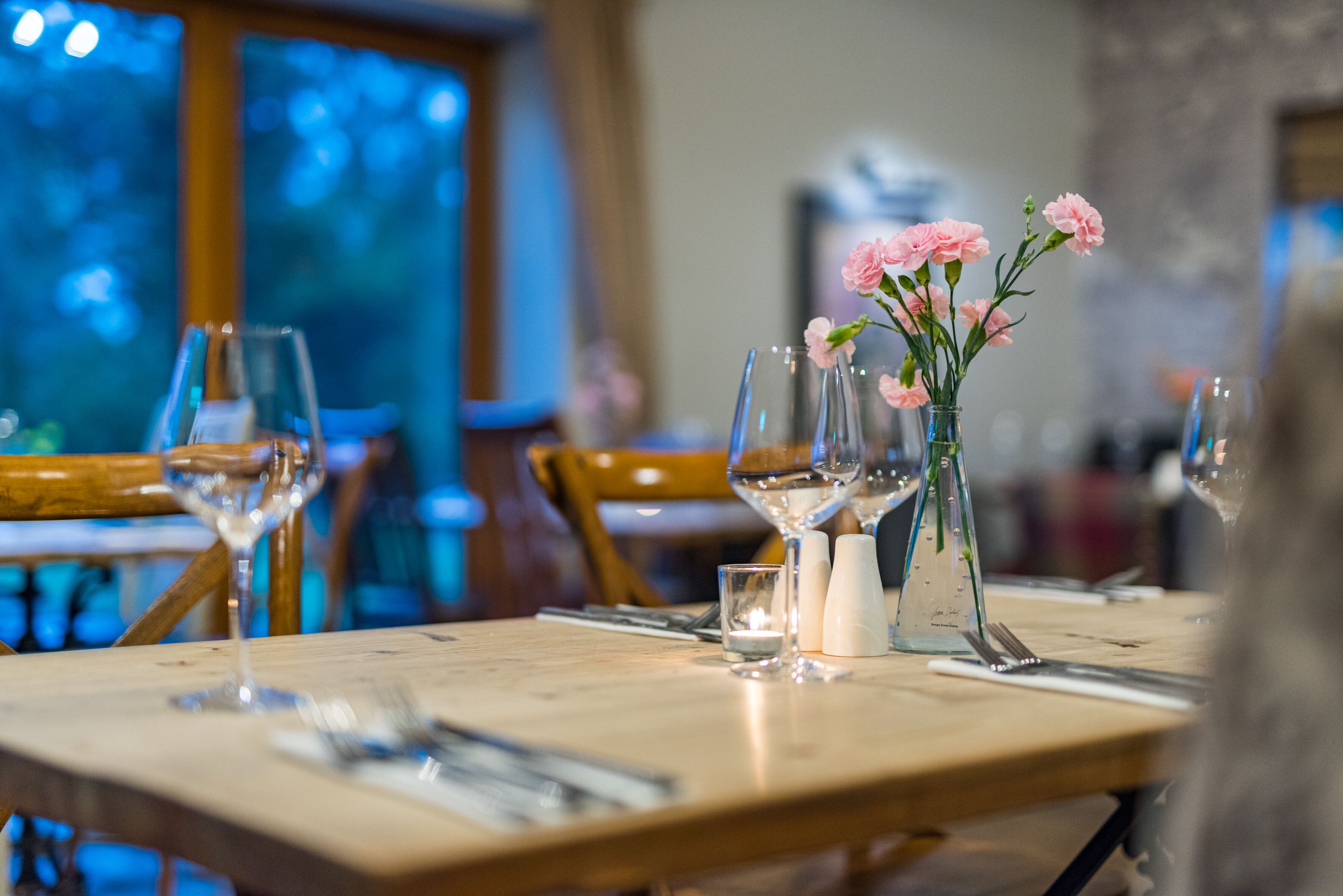 A dining table with a vase of pink flowers, salt and pepper shakers, and wine glasses.