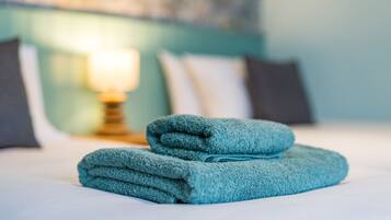 A neatly made bed with a folded teal towel and a bedside lamp.