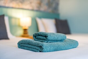 Una cama bien hecha con una toalla verde azulada doblada y una lámpara de noche.