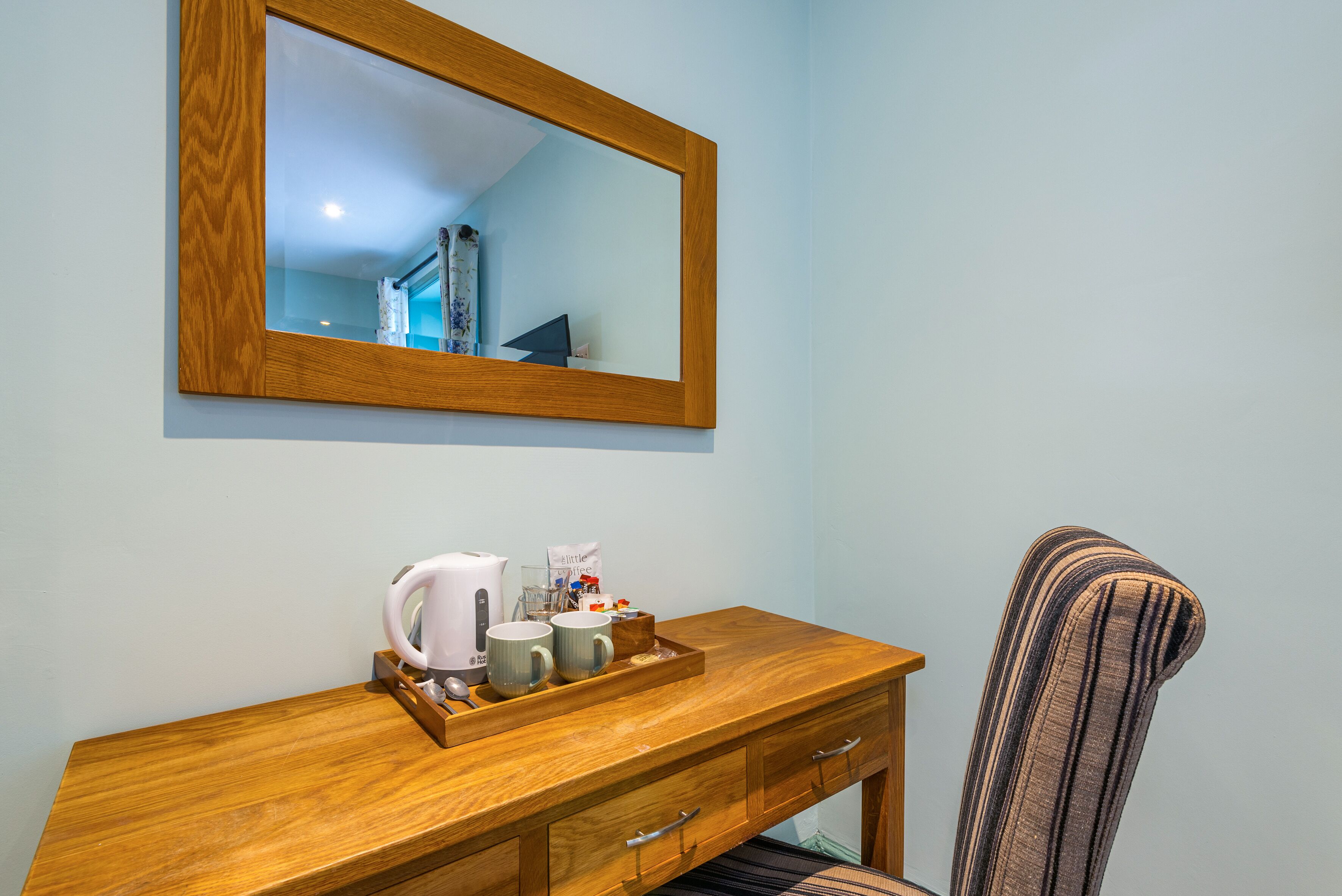 A wooden desk with a coffee maker, mugs, and a tray of items.