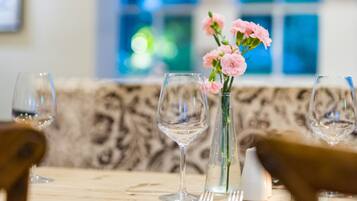 A dining table with a vase of pink flowers, wine glasses, and cutlery.