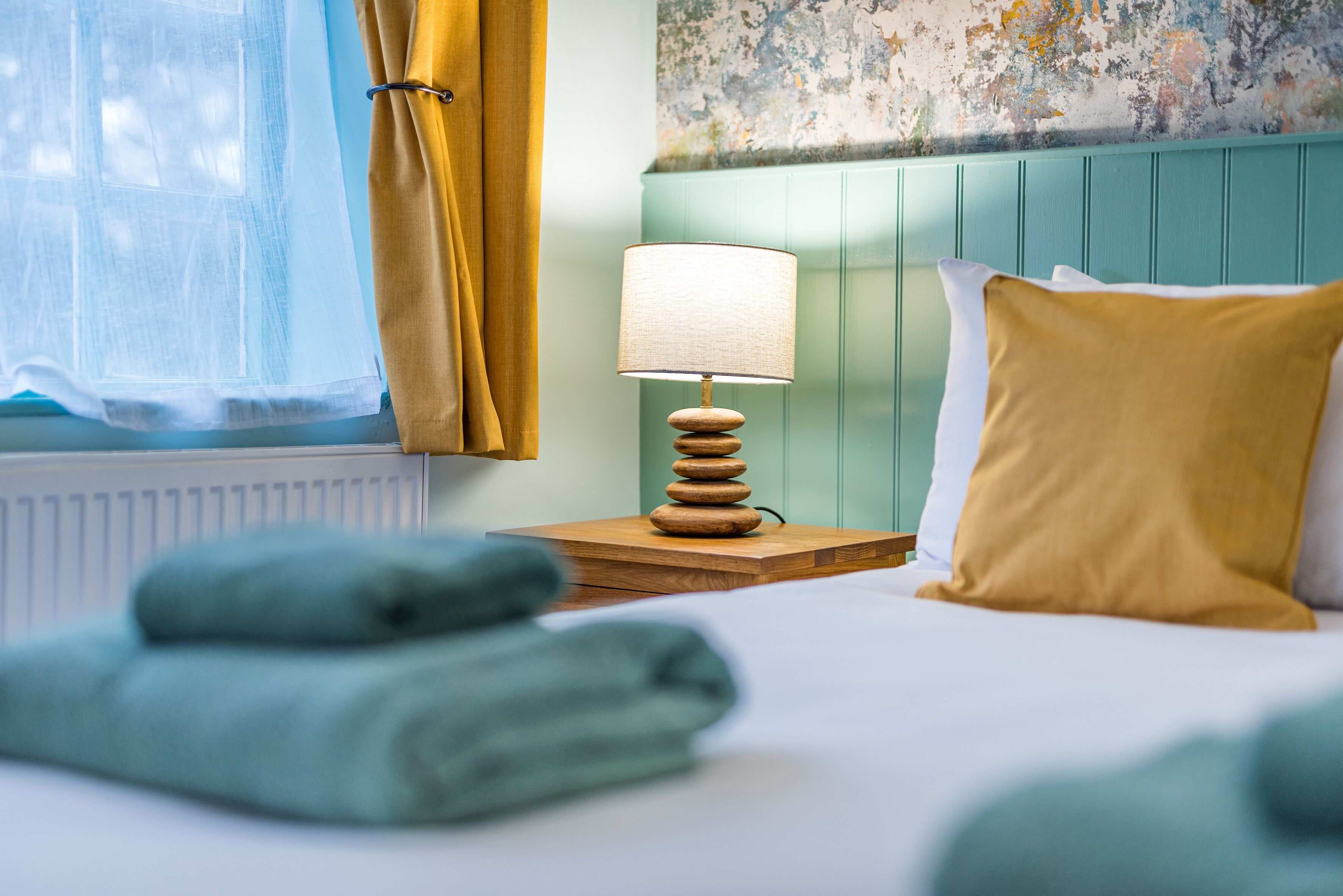 A neatly made bed with a wooden bedside table, a lamp, and a pillow.