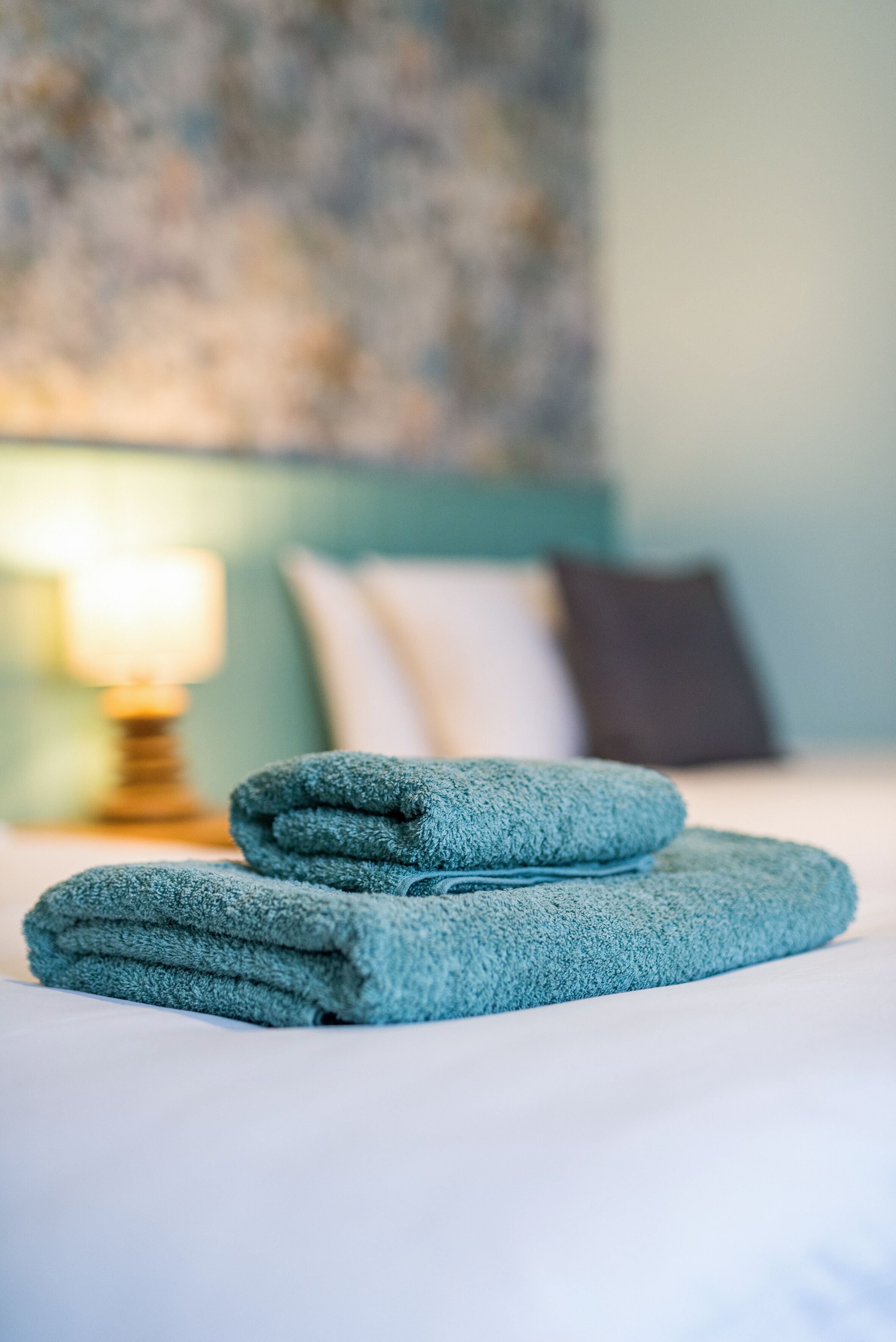 A neatly made bed with folded towels and a lamp in the background.