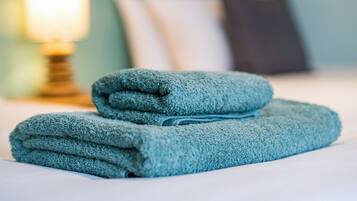 A neatly made bed with folded towels and a lamp in the background.