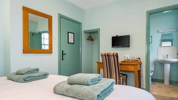 A hotel room with a bed, a wooden chair, a desk, a television, and a bathroom with a sink and mirror.