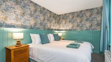 A bedroom with a bed, two bedside tables with lamps, a wooden nightstand, and a radiator.