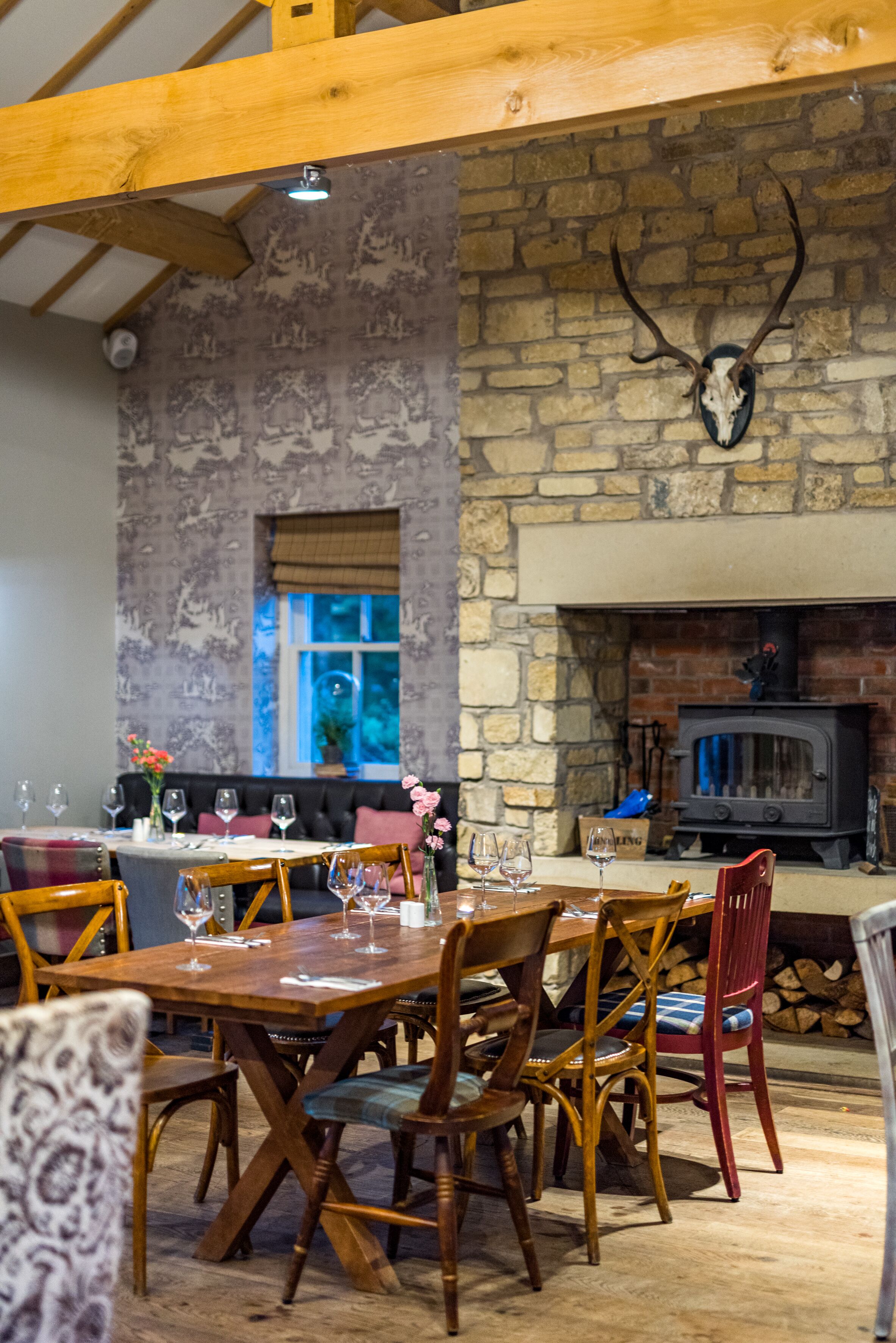 A dining area with a stone fireplace, wooden beams, and a mounted deer head.