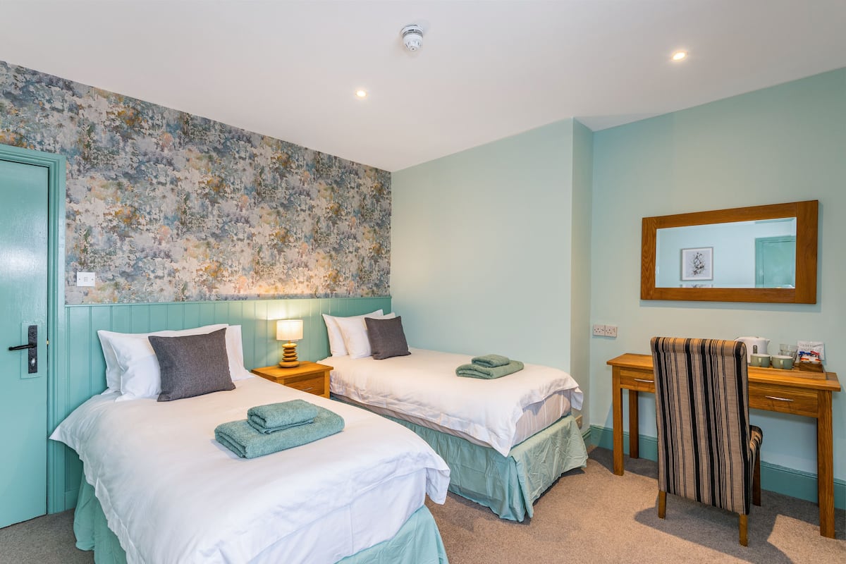 Une chambre d’hôtel avec deux lits, un bureau, une chaise et un miroir.