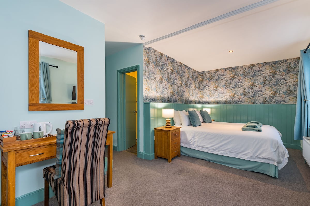 Une chambre à coucher comprenant un lit, une table de chevet, une lampe, une chaise et un bureau avec un miroir.