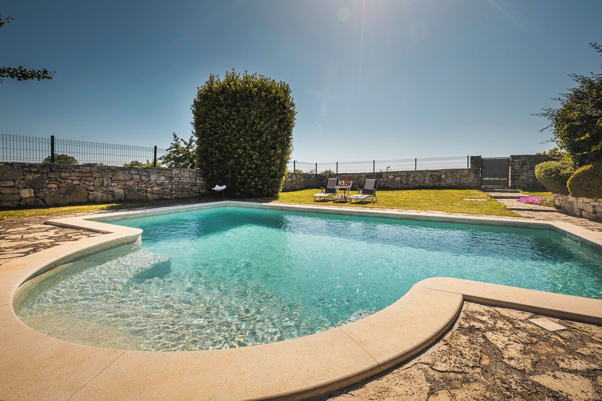 A swimming pool with a stone wall and a stone fence in the background.