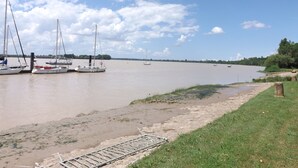 A calm river with boats docked on the left, a grassy bank on the right, and a clear sky above. - Maison a Louer Situé au Bord de la Dordogne (Saint-André-de-Cubzac)