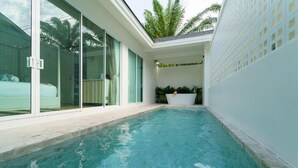 Ein Schwimmbecken mit Glasumrandung, einer weißen Außenwand und einem kleinen Gartenbereich mit Blumenkasten.