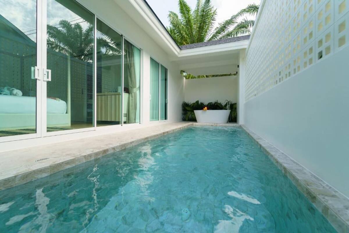 Une piscine dotée d’une enceinte en verre, d’un mur extérieur blanc et d’un petit espace jardin agrémenté d’un jardinier.