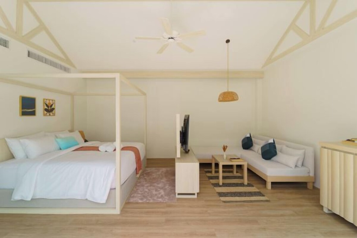 Een slaapkamer met een bed, een bank, een televisie en een plafondventilator.