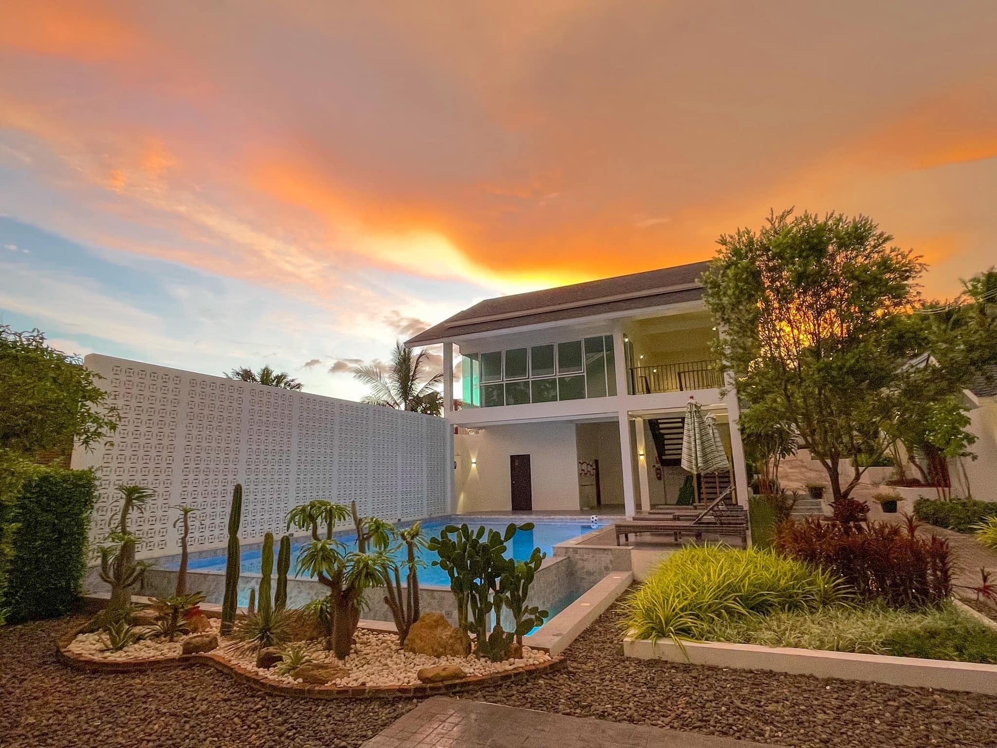 Una casa moderna con piscina, rodeada de plantas desérticas y un cielo al atardecer.