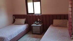 Un dormitorio con dos camas individuales, una mesita de noche y una ventana con persianas.