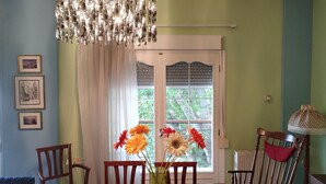 Una zona de dinar amb taula, cadires, un ram de flors, un llumí i una finestra amb cortines.