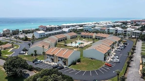 A coastal hotel with multiple buildings, a parking lot, and a pool area.