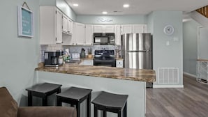 A modern kitchen with white cabinets, stainless steel appliances, and a granite countertop. There are three bar stools in the foreground.
