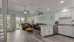 A spacious living area with a kitchen, featuring a ceiling fan, a dining table, and a sofa with cushions.