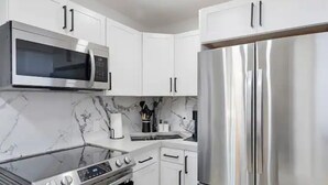 Eine moderne Küche mit weißen Schränken, einer Edelstahl-Mikrowelle, einem Backofen und einem Kühlschrank.