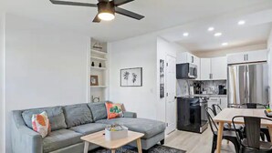 Ein modernes Wohnzimmer mit einem grauen Sofa, einem Holztisch und einem Deckenventilator.