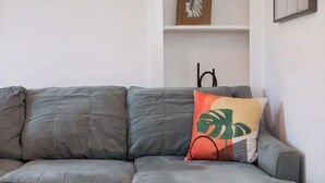 Ein graues Sofa mit einem einzelnen Zierkissen mit tropischem Blättermotiv.