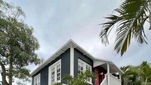 Ein zweistöckiges Haus mit Balkon, umgeben von Grün und Palmen.