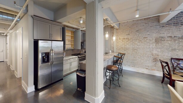 A modern kitchen with stainless steel appliances, a brick wall, and a dining area with a round table and chairs. - 60 Night Minimum Rental - FQ Apt. 2B/2B (New Orleans)